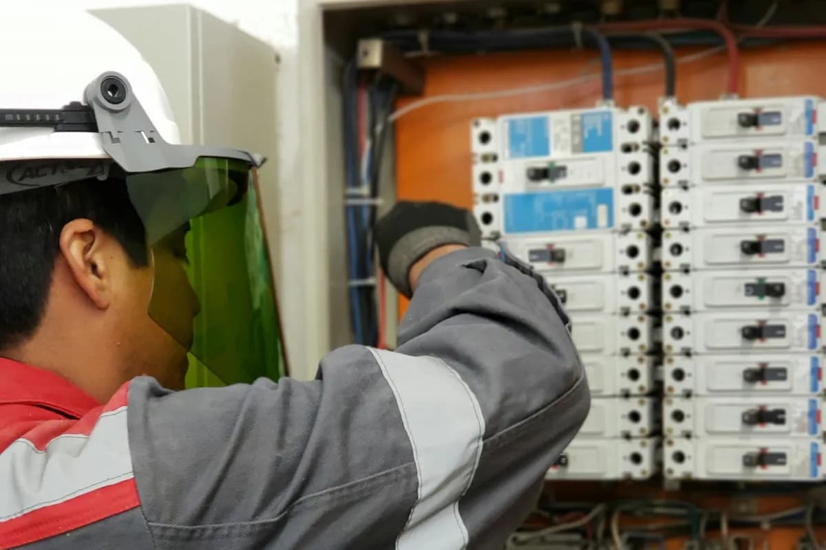 Electrician in a face shield testing a live distribution board
